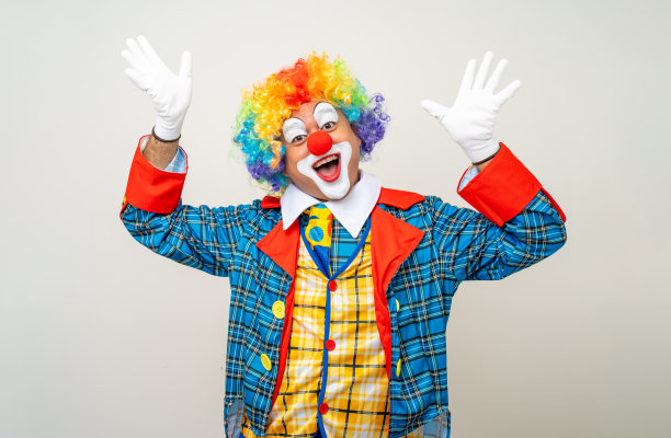 小丑先生。滑稽的震惊脸喜剧演员小丑的肖像，穿着五颜六色的服装，戴着假发，站着摆姿势，对着镜头微笑。在孤立的背景下，快乐的表情让人惊讶。图片下载