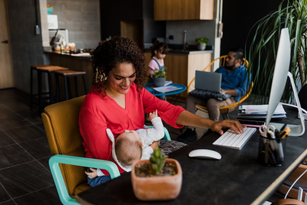 年轻的拉丁母亲在家里用电脑工作，同时在墨西哥给她的儿子喂奶拉丁美洲，家庭办公室概念，西班牙裔家庭图片下载