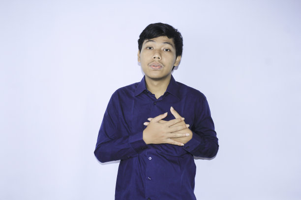 一名年轻的亚洲男子穿着海军蓝衬衫，正从心脏病发作的疼痛中放松下来，做着吸气和呼气，面部表情和手势图片下载