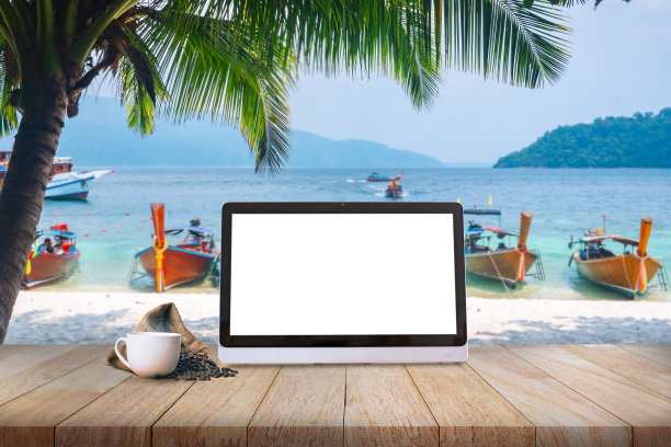 在椰树环绕的海边，木桌上放着笔记本电脑和咖啡杯，代表着旅行和数字游牧民族的概念。图片下载