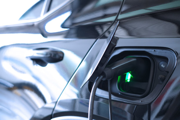 电动插头电缆连接充电站和正在充电的电动汽车。图片下载