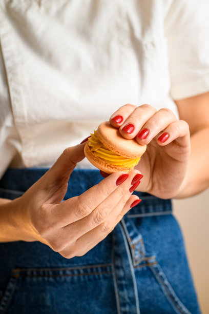 红色美甲师的手连接两半马卡龙，用甘纳许装饰图片下载