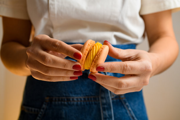 糖果师的手与红色指甲连接两半马卡龙，装饰有甘纳许，正面视图图片下载