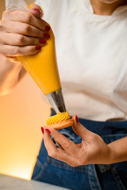 手里拿着糖果袋的女人把美味的奶油馅挤进新鲜的马卡龙壳里图片下载