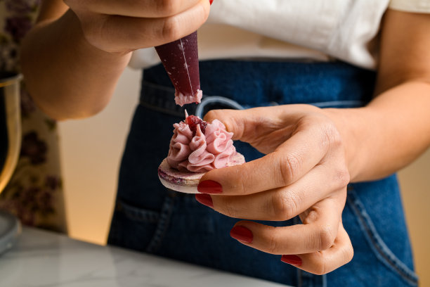 女厨师将糖果袋里的果酱挤进半块马卡龙上的甘纳许奶油里，特写图片下载