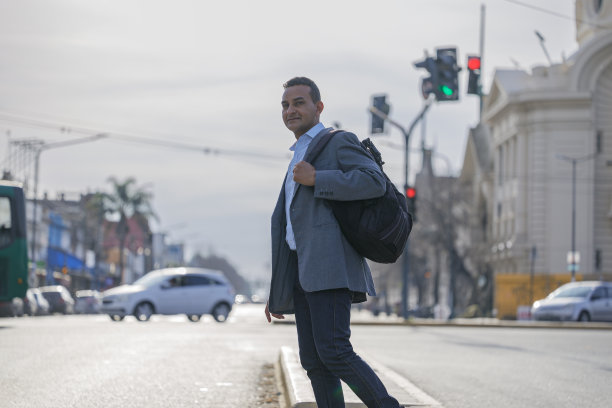 穿着西装背着背包的拉丁裔男子在一个有复印空间的城市穿过街道。图片下载