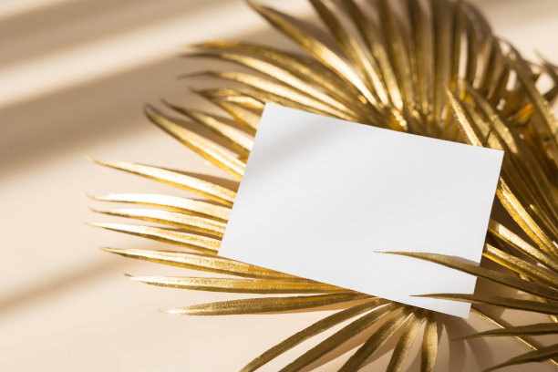 邀请卡模型与金色棕榈叶米色粉彩背景。俯视图，平面布局，复制空间。模板空白的白纸模型为品牌和广告图片下载