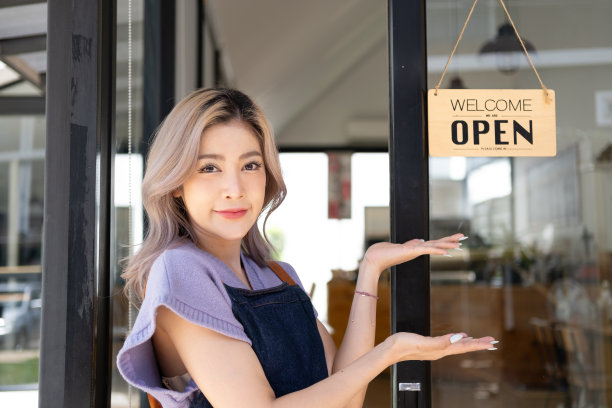 快乐的年轻老板女服务员站在餐厅咖啡店店门口欢迎顾客，小生意年轻的亚洲老板零售，咖啡店与开放板的标志图片下载
