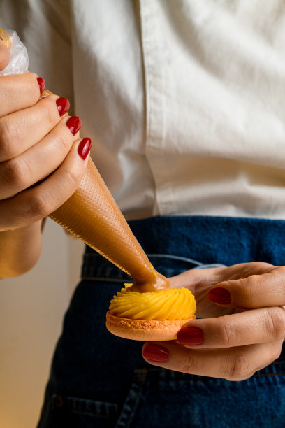 女人的手拿着糖果袋，把橙子奶油挤到新鲜马卡龙的一半图片下载