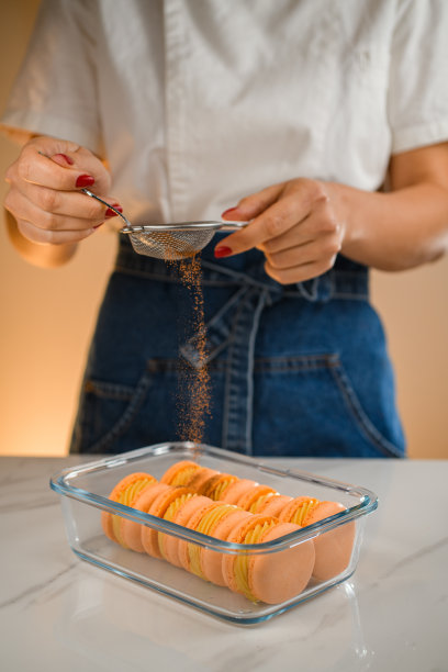 女厨师用筛子在刚做的法式马卡龙上撒上肉桂。特写视图。图片下载