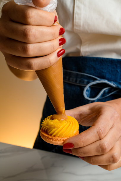 一个女人手里拿着糖果袋，把桔子奶油挤到新鲜的马卡龙里图片下载