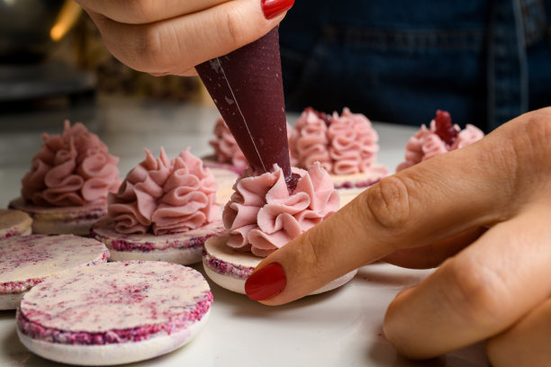 女厨师将果酱挤进半块马卡龙上的甘纳许奶油里，特写图片下载
