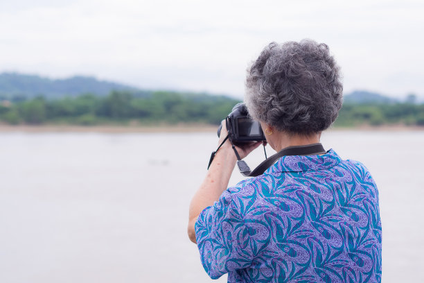 老妇人在河边用数码相机拍照。图片下载