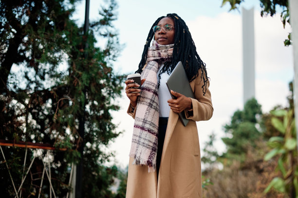 一个自由职业者拿着咖啡和笔记本电脑走在咖啡馆前。图片下载