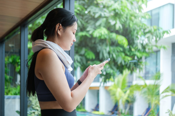 一名穿着运动服的年轻女子在健身中心锻炼后休息时使用手机。图片下载