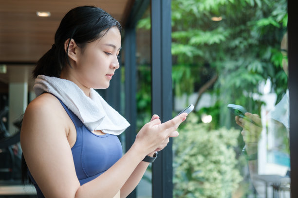 穿着运动服玩智能手机的美女，在健身房训练后放松。图片下载