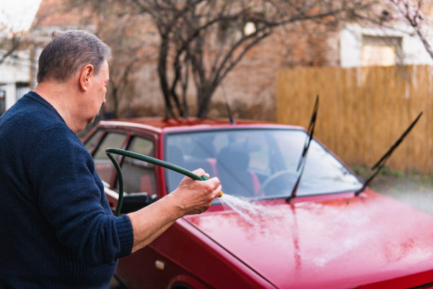 一位年长的男子手里拿着水管，在后院洗车。图片下载