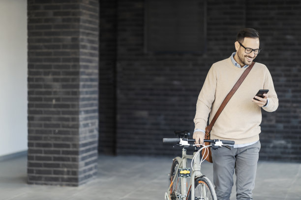 一个快乐的男人把自行车推到外面，一边打字，一边对着电话微笑。图片下载