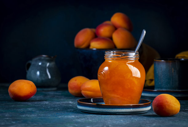 杏果酱或配置在玻璃罐与勺子，新鲜水果在蓝色的桌子背景图片下载