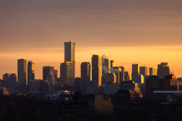 日出时多伦多市中心的天际线，金色的光线照亮了天空和建筑物的侧面图片下载