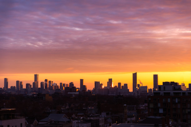 日出时多伦多市中心的天际线，金色的光线照亮了天空和建筑物的侧面图片下载
