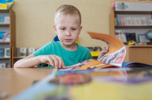 图书馆里的男孩。7岁的乌克兰男孩正坐在图书馆的一张桌子上看书。学习观念正常，求知欲强，渴望学习新事物。模糊的背景和字母图片下载