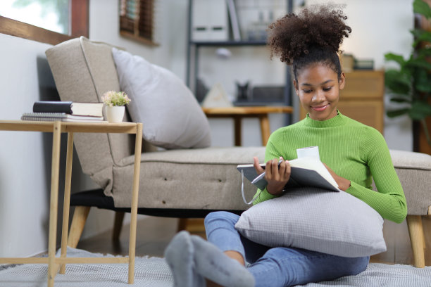 轻松美丽的非洲女人在家里的客厅看书。图片下载