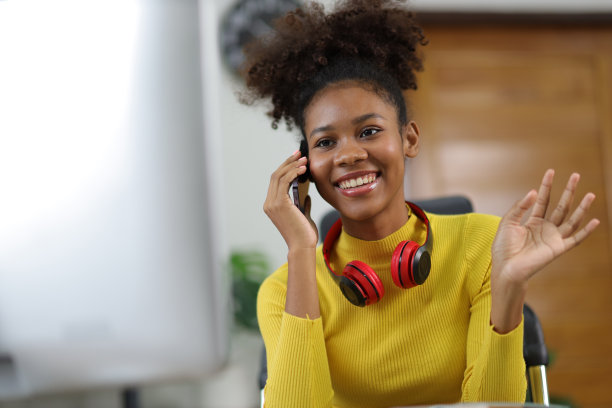 年轻美丽的非洲女人在家庭办公室用智能手机和别人打电话。图片下载