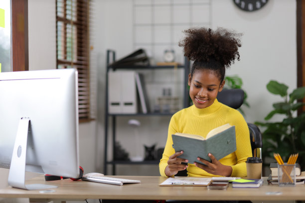 年轻的非洲妇女在家里用电脑和看书准备考试。图片下载