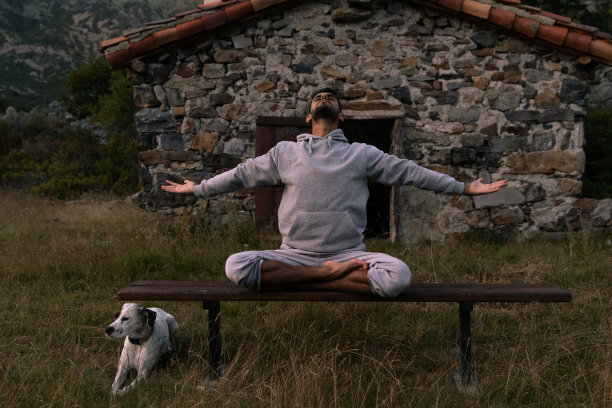 穿着灰色运动衫的年轻印度男子在野外冥想时练习瑜伽，伸展双臂——人们在户外冥想的照片。图片下载