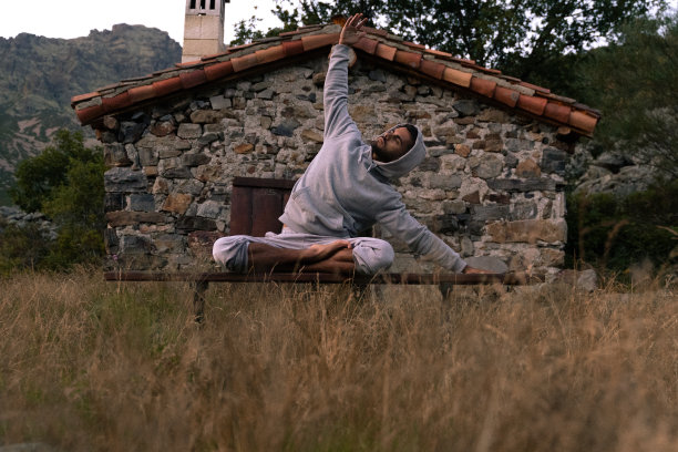 一名穿着灰色运动衫的年轻印度男子一边练习瑜伽，一边伸展双臂，一边在石头遮蔽处冥想——人们在户外冥想的照片。图片下载