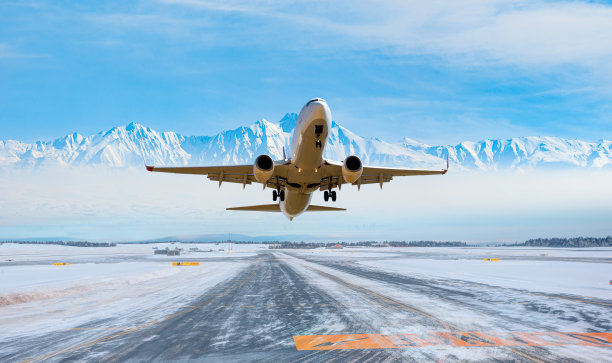 客机起飞时飞过雪山跑道，背景是白雪覆盖的机场图片下载