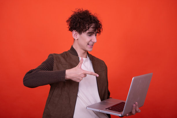 拿着笔记本电脑摆出橙色背景的搞笑人。图片下载