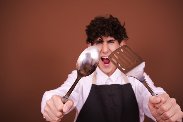 拿着金属勺子的年轻有趣的厨师。图片下载