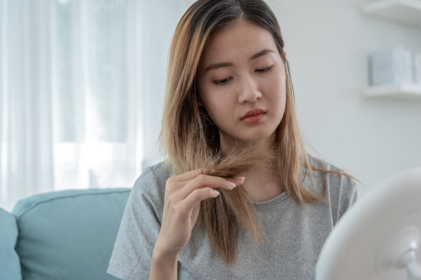 亚洲女性看着受损的头发，脱发，头发稀疏的问题，维生素缺乏，秃顶，产后，生物素，锌，月经或内分泌紊乱，荷尔蒙失衡非常悲伤和不安图片下载