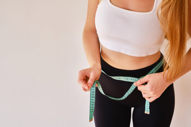 年轻女子细腰上系着一根卷尺。健身教练。营养、训练和正确生活方式的概念。美容与减肥图片下载