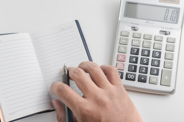 男人的手写在笔记本上，计算器和笔在白色背景上图片下载