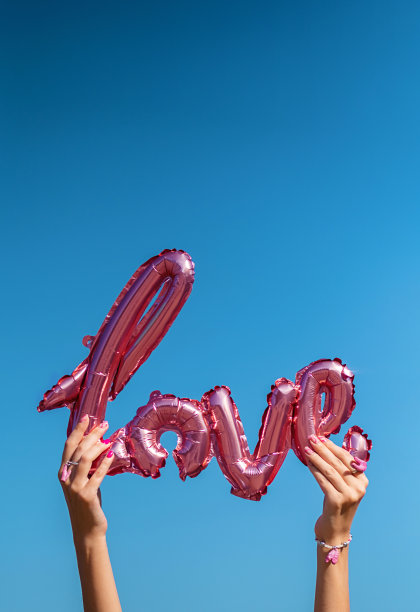 女性手持爱字气球对着蓝天。图片下载