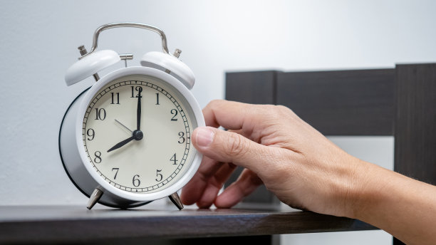 时间管理理念。男手把白色闹钟放在桌子上。图片下载