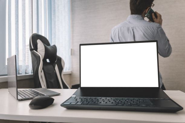 白色办公室里的笔记本电脑，背景是一个正在打电话的员工。图片下载