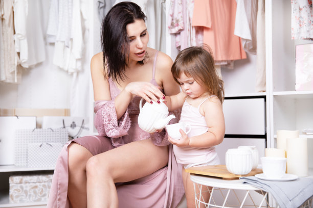 清晨，年轻美丽苗条的母亲和她的小女儿在明亮的更衣室里玩耍。图片下载