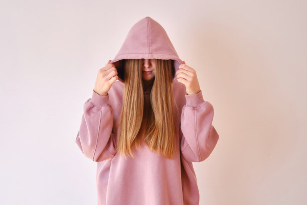 年轻漂亮的女孩穿着粉色卫衣摆姿势。温暖的超大连帽衫与兜帽。时尚新潮的潮人蝴蝶结。在商店里试穿衣服。青年亚文化。时尚服装广告图片下载