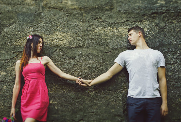 相爱的情侣是牵手在古老的古镇里。身穿粉色连衣裙的女孩和穿着短裤的男子站在中世纪石墙附近。浪漫的夏天时髦的照片。图片下载