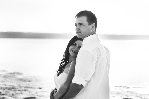 新婚夫妇在海滩上拥抱。阳光明媚的夏日照片。新娘披散着头发，穿着露肩裙。海洋浪漫的仪式。海边的爱情故事。沙子，水和地平线。蜜月。图片下载