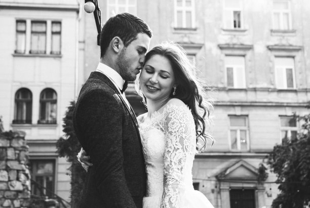 新婚夫妇在老城拥抱。质朴的新娘披散着头发，挽着身穿灰色西装、打着领结的新郎的脸。中世纪古镇的爱情。白色蕾丝婚纱。经典的黑白照片。图片下载