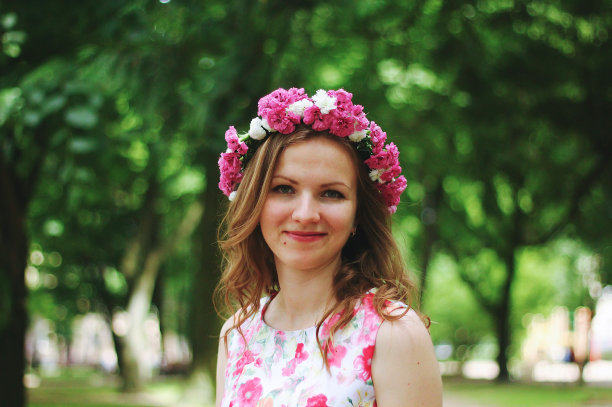 美丽的女孩戴着粉红色的花冠在绿色的夏日公园向你微笑。粉红色的花裙和翡翠树。春天的女人照片。国际妇女节和母亲节假期。花花冠。图片下载