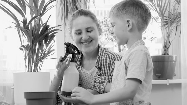 黑白照片，母亲给小儿子洒水器，让他给家里的花草浇水图片下载