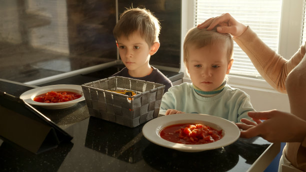 年轻的母亲在餐桌上为孩子们准备汤。家常菜，在家做饭，孩子健康营养。图片下载