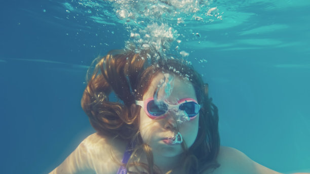 年轻的白人女孩在游泳池里潜水，呼出气泡图片下载