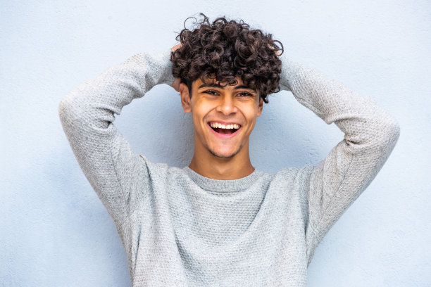 在蓝色背景下，快乐的年轻北非男子笑着双手放在脑后图片下载